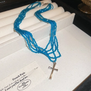 Close-up of a five-layer bright blue beaded necklace featuring a silver cross pendant