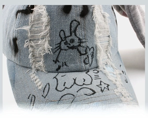Detailaufnahme der hellblauen Jeanskappe mit Rissen, Graffiti-Print und Hasenohren-Motiv