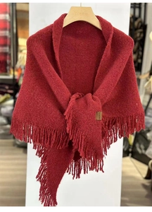 Detail of red wool shawl with fringe edges hanging on a wooden hanger in shop