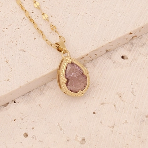 Close-up of gold heart owl pendant with pink teardrop gemstone and refined metal chain