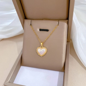 Detailed view of a gold heart pendant with iridescent stone in a beige jewelry gift box