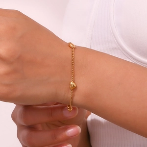 Close-up of a gold heart charm bracelet on a model's wrist with polished curb chain links