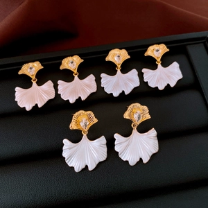 Close-up of elegant ginkgo leaf earrings with gold stem and white enamel inlay detail