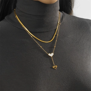 Detail of a layered gold necklace with white heart pendant on a gray knit sweater