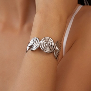 Close-up of three polished silver spiral discs on a sleek metal open cuff bracelet