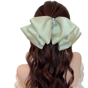 Detail of oversized sage green satin bow hair clip with pearls on long wavy hair