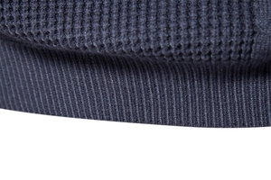 Macro detail of dark grey waffle knit texture and ribbed hem on a men's winter sweater