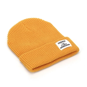 Detail of a yellow ribbed knit beanie with a white fashion text label and folded cuff