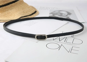 Detail view of a slim black leather belt with a matte oval metal buckle on a magazine