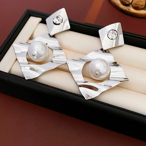 Macro detail of geometric silver diamond earrings with elegant white faux pearls