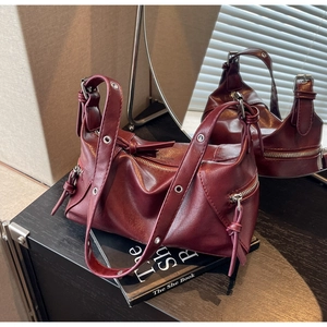 Detail view of burgundy leather tote bag with metal zippers and eyelets on black surface