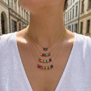 Detail of layered gold necklaces with marquise rainbow zircons on white linen shirt
