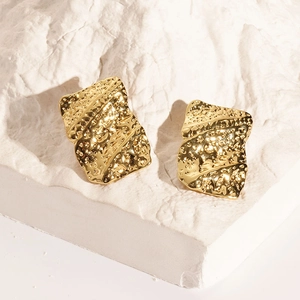 Macro view of gold irregular textured square earrings on white mineral rock base