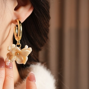 Detail of elegant gold hoop earrings with cream resin flower petals on a model