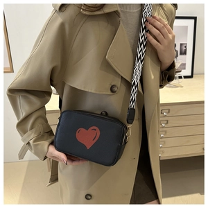 Close-up of black lychee leather crossbody bag with red heart and patterned wide strap