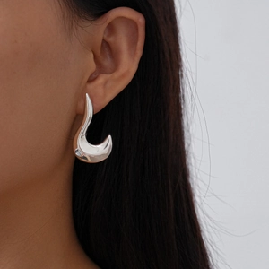 Macro shot of silver irregular geometric metal earring on model showing smooth fluid design