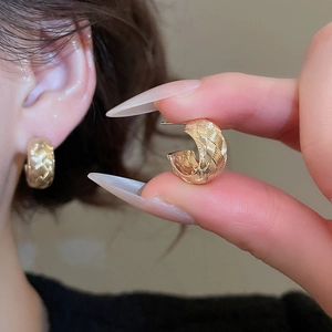 Detailed macro view of gold-colored woven texture C-shape earrings with a layered design
