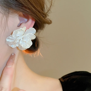 Close-up of white acrylic flower earrings with pearl center detail on model ear