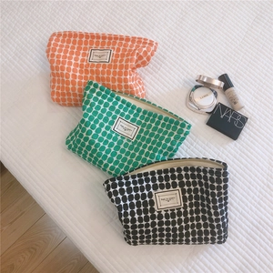 Three colorful geometric cotton makeup pouches shown with luxury cosmetics on a bed