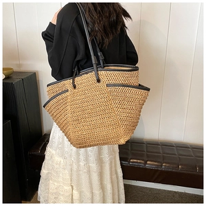 Detail of large woven straw tote with black leather straps on a model's shoulder