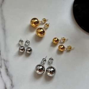 Polished gold and silver ball stud earrings in small and large sizes on marble surface