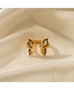 Detail of gold butterfly ring with black stones and hollow engraving on silk background