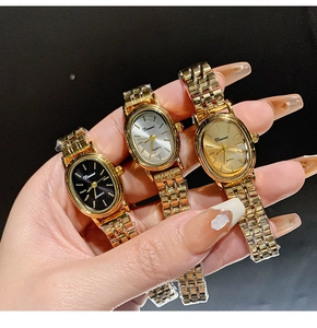 Close-up of three gold quartz watches with black, white and gold oval dials held in hand