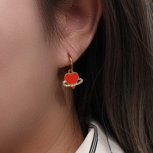 Close-up of golden hoop earrings with red enamel heart pendants and zircon-studded Saturn rings