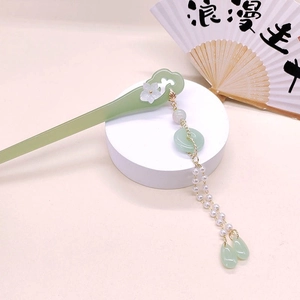 Detail of green acetate hair stick featuring white flower motifs and elegant tassels