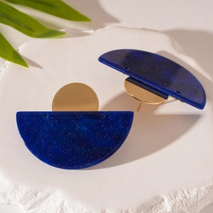 Detailed shot of half-round blue acrylic earrings with gold metal accents on stone