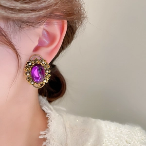 Close-up of vintage purple oval crystal earring with ornate gold floral details on ear