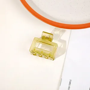 Detail of a translucent yellow rectangular hair claw clip on a minimal white background