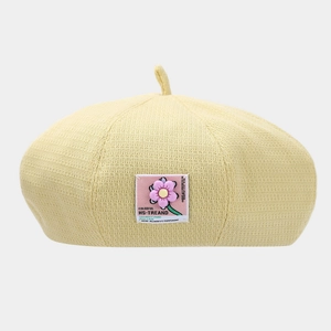 Detail of light yellow knitted beret featuring a colorful floral fabric patch decoration