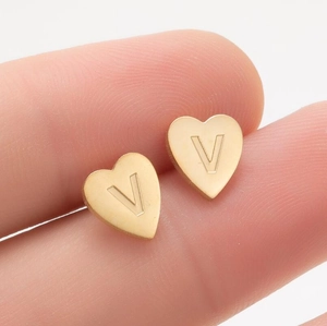 Vue macro d'une boucle d'oreille cœur dorée avec une lettre V gravée au style minimaliste