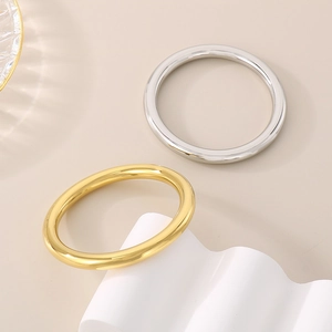 Minimalist high-polish stainless steel bangles in gold and silver finish shown on a pedestal