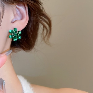 Close-up of a model wearing emerald green floral stud earrings with zircon accents
