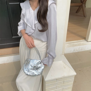 Silver sequin shoulder bag held by a model in a purple shirt and white pleated skirt