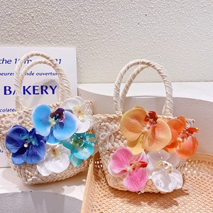Detail of beach straw handbag featuring colorful orchid flowers and pearl chain handle
