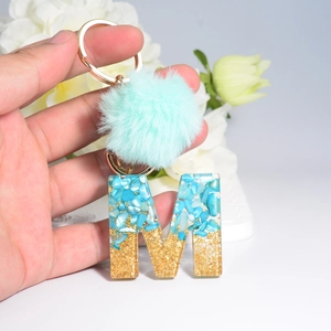 Letter M keychain with turquoise stones, gold glitter, and light blue faux fur pompom