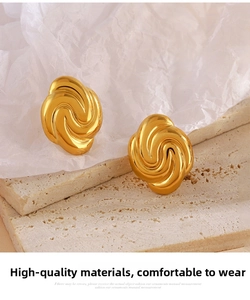 Macro detail of 18K gold plated geometric spiral stud earrings on a textured stone base