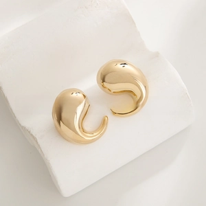 Macro shot of polished gold-plated waterdrop earrings on a minimalist stone surface