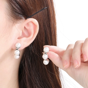 Detail view of C-shaped stainless steel earrings with three white pearls on a model