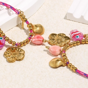 Gros plan détaillé des breloques coquillage et fleur dorées 18K sur bracelets tissés