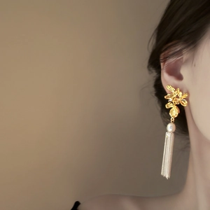 Détail de boucles d'oreilles fleur dorée avec perle élégante et longues franges en métal