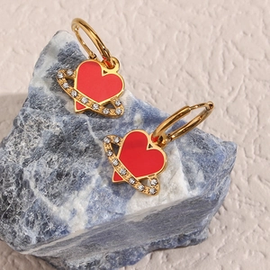 Macro shot of gold-plated red heart earrings with zircon stones on natural mineral rock
