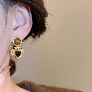 Close-up of heart-shaped gold earring with tiger eye stone and black inlay on model