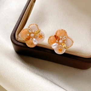 Macro shot of clover pearl earrings with orange zircons on a leather jewelry box