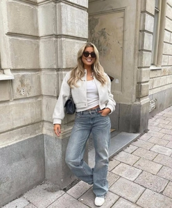 Detail of a white cropped tweed jacket and blue denim jeans with a black quilted chain bag