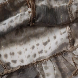 Detail of taupe tie-dye chiffon fabric with gold metallic thread and ruffled edges