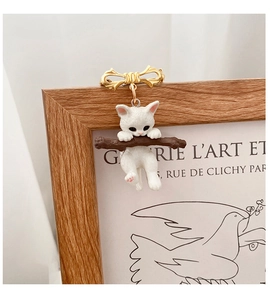 Detailed view of a cute white cat on a branch brooch with a golden bow accent